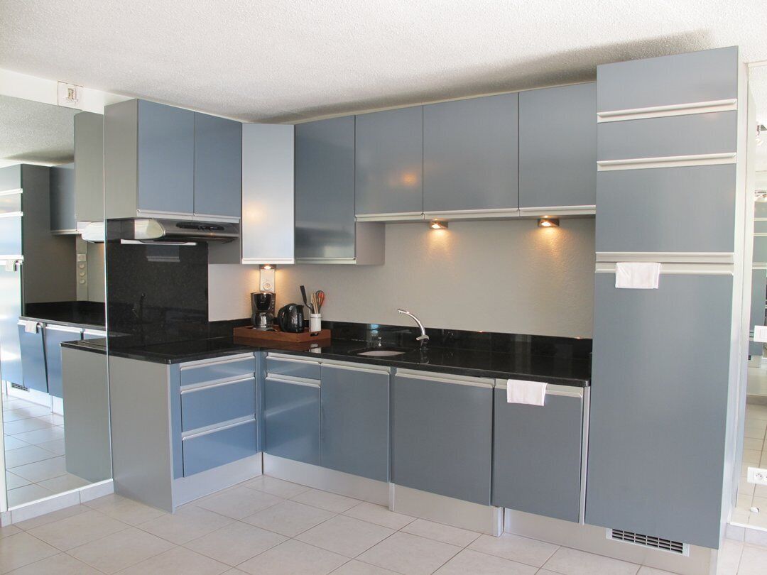 A modern kitchen with grey cabinets, a black countertop, and a stainless steel sink.