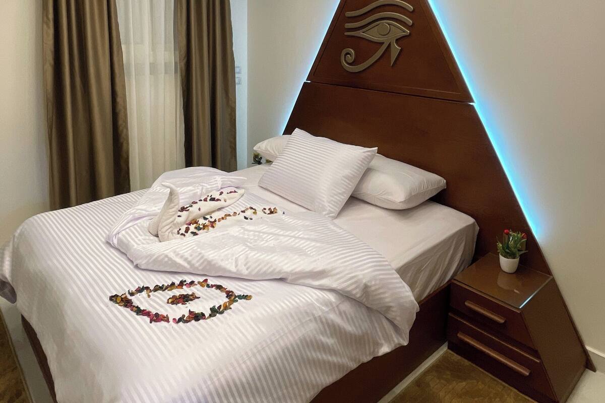 A modern hotel room with a neatly made bed, a decorative headboard, and a geometric ceiling design.