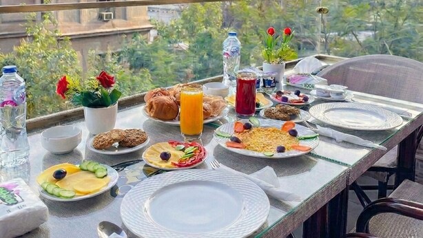 A dining table with food and drinks, overlooking pyramids and greenery. - Queen Inn Pyramids View (Giza)