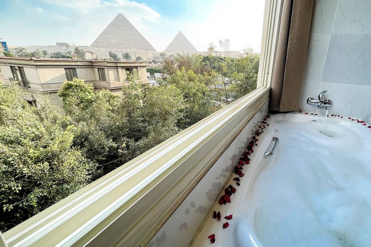 A bathroom with a bathtub, a window, and a view of the pyramids.