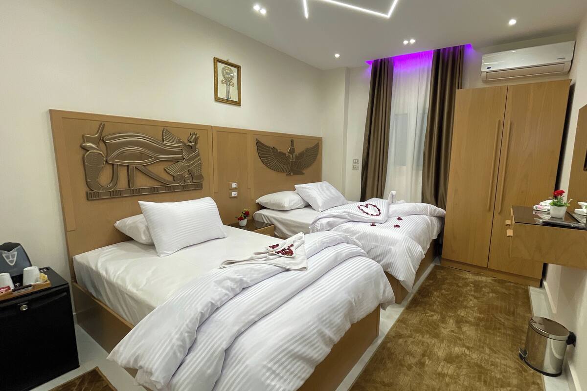 A hotel room with two beds, a wooden headboard with decorative carvings, a mounted TV, and an air conditioning unit.