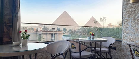 A balcony with a glass table and chairs, a view of the pyramids, and a stone wall.