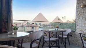 A balcony with a glass table and chairs, a view of the pyramids, and a stone wall. - Queen Inn Pyramids View (Giza)