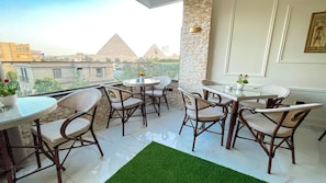 A balcony with a glass table and wicker chairs, a green rug, and a view of pyramids. - Queen Inn Pyramids View (Giza)