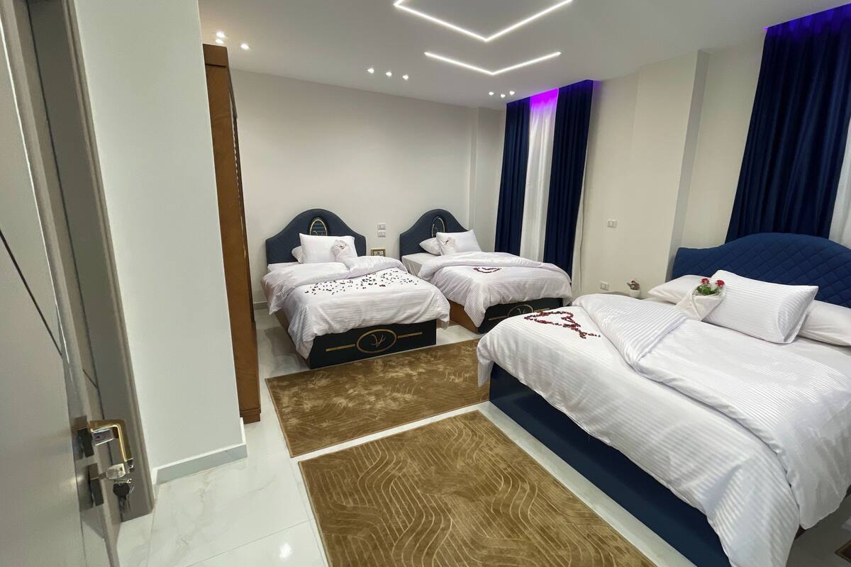 A hotel room with two beds, a wooden floor, and a modern ceiling design.