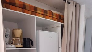 Une cuisine compacte avec un réfrigérateur blanc, un four à micro-ondes, une machine à café et un petit tabouret.