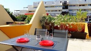 A rooftop terrace with a table set for two, surrounded by potted plants and a view of a residential building. - GENTLEMAN - Studio Héliopolis D 84 - Luxury - 2 people (AGDE)