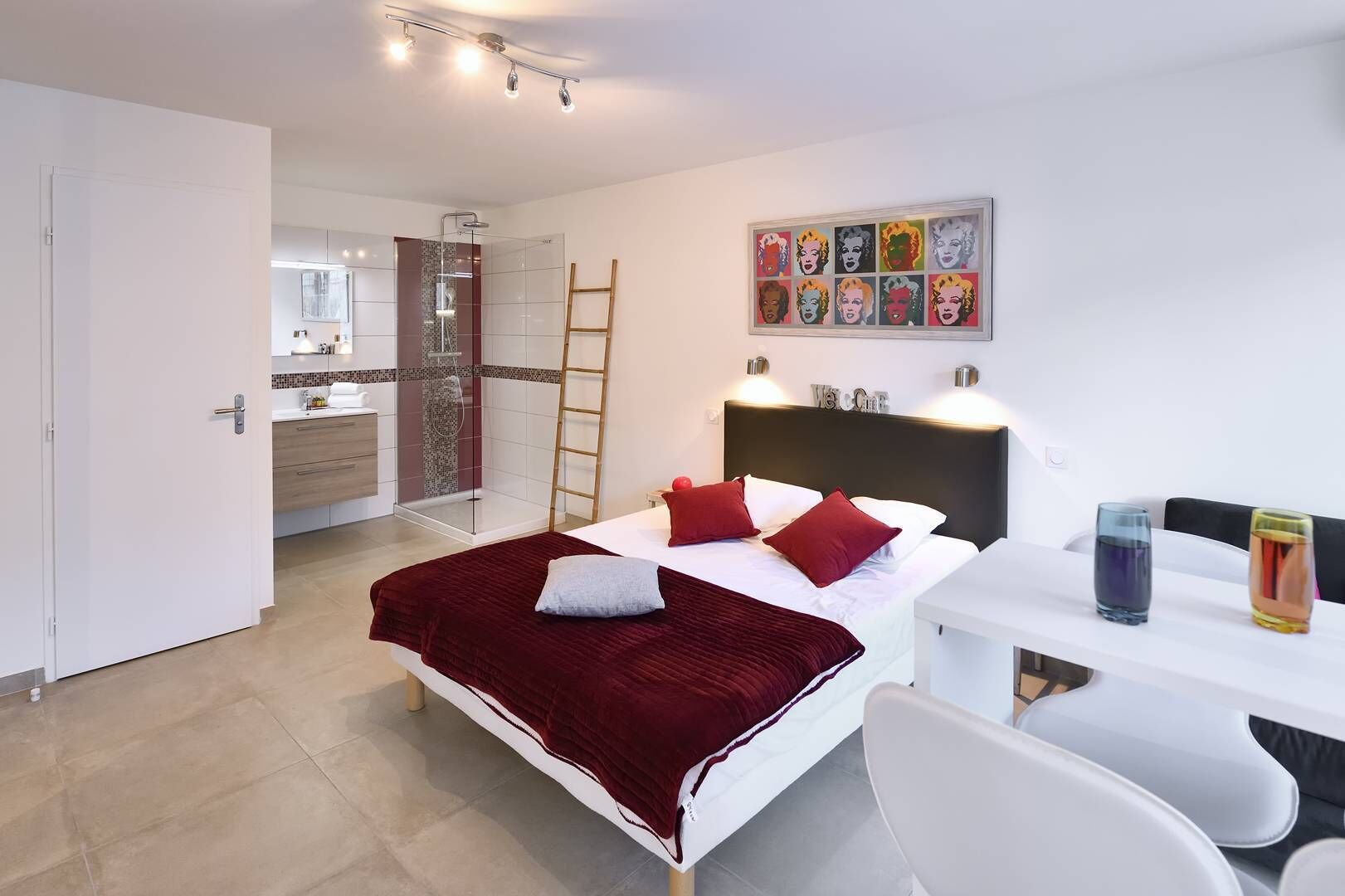 Habitación de hotel moderna con cama, escritorio y silla, zona de ducha y baño visible a través de una puerta abierta.