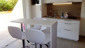 A compact kitchen with a white countertop, a sink, and a microwave. There are two white chairs and a small table. - GENTLEMAN - Studio Héliopolis D 84 - Luxury - 2 people (AGDE)