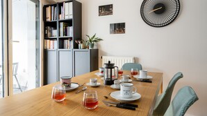 Ein Essbereich mit einem Holztisch, gedeckt für Tee, einem Bücherregal und einer Wanduhr mit Stadtansicht.