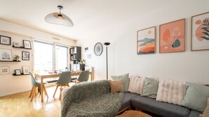 Ein modernes Wohnzimmer mit einer Couch, einem Esstisch, Stühlen und einem großen Fenster.