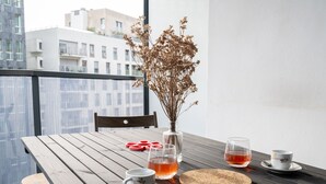 Ein Holztisch mit einer Vase getrockneter Blumen, zwei Teetassen und einer Tasse auf einem Balkon mit Blick auf die Stadt.