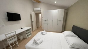 Ein Schlafzimmer mit Bett, Schreibtisch, Stuhl, Fernseher und Kleiderschrank.