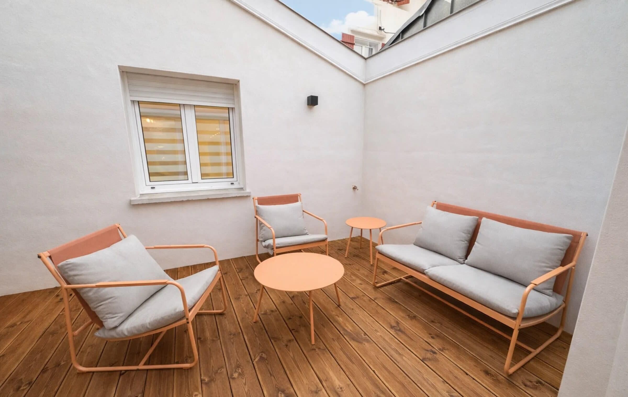 A small, enclosed patio area with a wooden floor, a sofa, two chairs, and a small table.