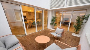 Eine Terrasse im Freien mit Holzboden, einem runden Tisch und zwei gepolsterten Stühlen.