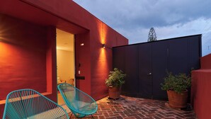 A patio with two blue chairs, a red wall, and a dark gate.