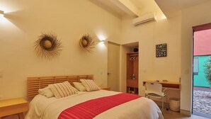 A bedroom with a wooden bed, a desk, and a chair. There is a small trash bin and a coat rack.