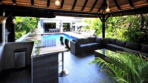Zona de piscina al aire libre con bar, asientos y vistas a un edificio al fondo.