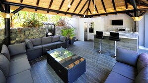 Un espacio exterior moderno con pared de piedra, cocina integrada y zona de estar con una mesa de centro de vidrio.