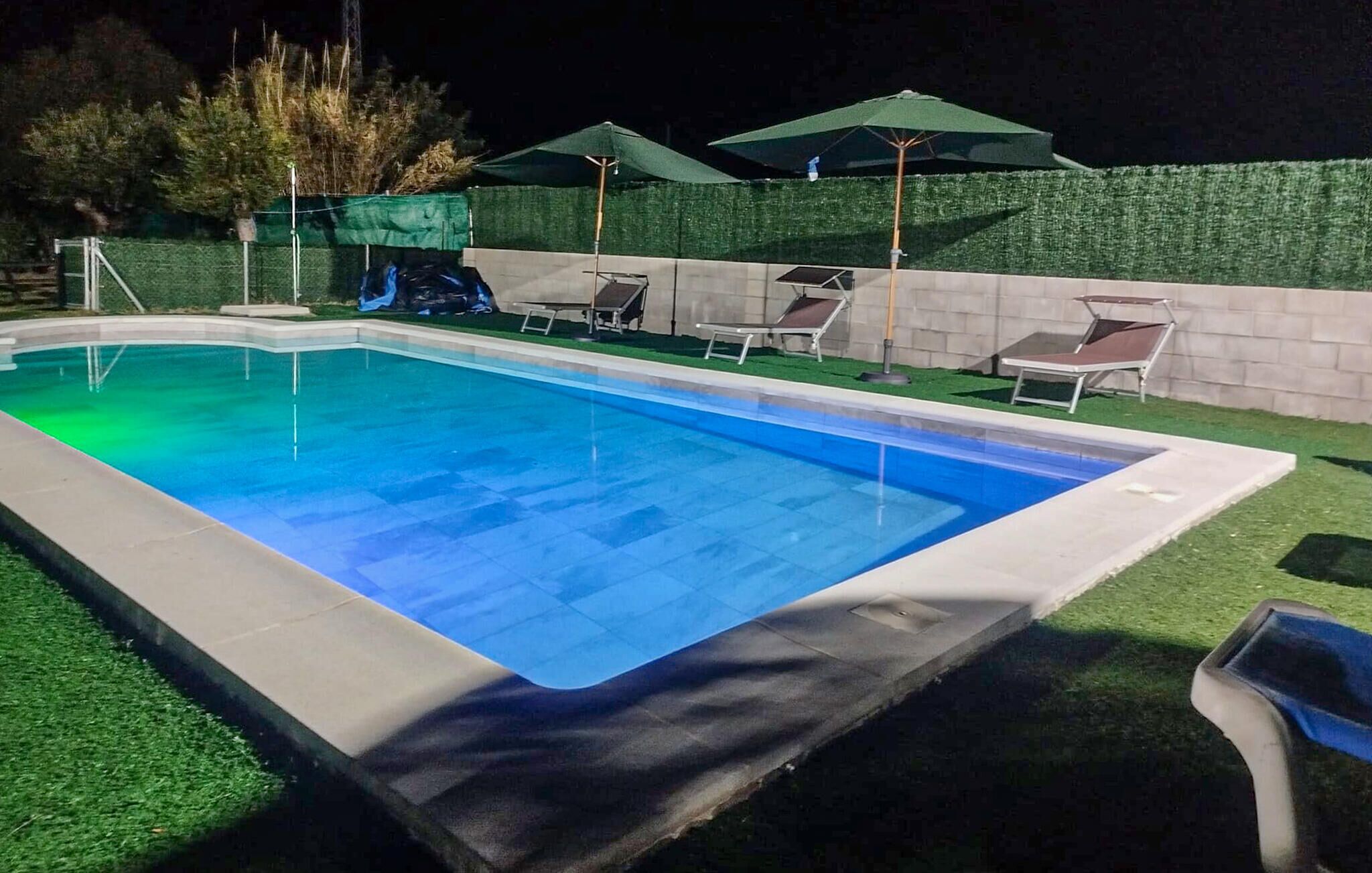 En rektangulär swimmingpool med en kant av kakel, omgiven av konstgräs och en låg stenmur.