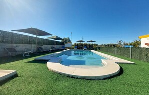 Een zwembad met kunstgras, ligbedden en parasols.