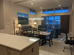 Ein modernes Wohnzimmer mit Essbereich, einer Couch, einem Couchtisch und einem großen Fenster mit Blick auf den Himmel.