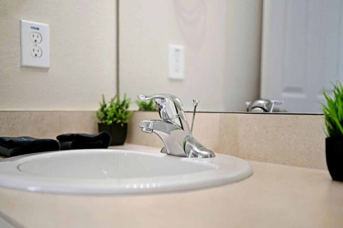Un lavamanos de baño con un grifo moderno, una planta en maceta y un espejo.