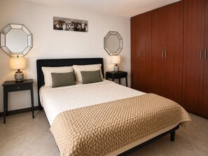 A bedroom with a bed, two nightstands, a wooden wardrobe, and two wall mirrors.