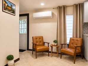 A living room with two leather armchairs, a small table with a plant, and a window with curtains.