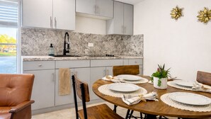 Une cuisine moderne avec des meubles gris, un plan de travail en granit et un coin repas avec une table en bois, mise pour quatre personnes.