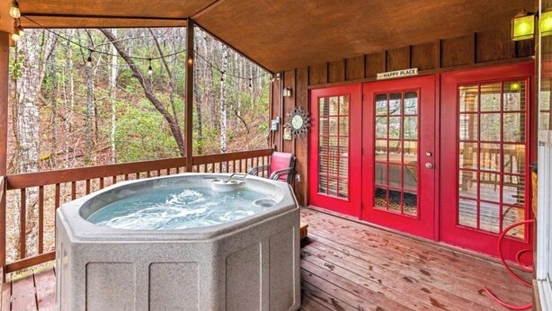 A wooden deck with a hot tub, red doors, and a sign reading "HAPPY PLACE". - Teaberry. This is a cozy mountain retreat-peaceful setting, easy access to town. (Gatlinburg)