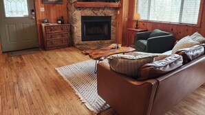 A cozy living room with a stone fireplace, wooden walls, a television, and a comfortable couch. - Teaberry. This is a cozy mountain retreat-peaceful setting, easy access to town. (Gatlinburg)