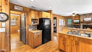 A wooden cabin-style kitchen with a black refrigerator, wooden cabinets, a stone fireplace, and a sink. - Teaberry. This is a cozy mountain retreat-peaceful setting, easy access to town. (Gatlinburg)