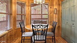 A wooden-paneled room with a round table and four chairs, a chandelier, and a door with a light switch. - Teaberry. This is a cozy mountain retreat-peaceful setting, easy access to town. (Gatlinburg)