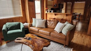 A wooden interior with a leather sofa, a green armchair, and a wooden coffee table. - Teaberry. This is a cozy mountain retreat-peaceful setting, easy access to town. (Gatlinburg)