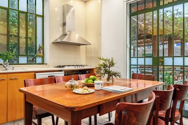 A dining area with a wooden table, chairs, a stove, and a window with a view of greenery.