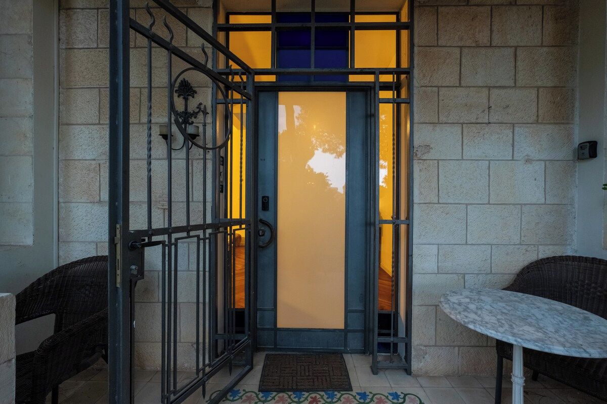 A hotel entrance with a metal gate, a blue door, and a small table with a chair outside.