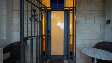 A hotel entrance with a metal gate, a blue door, and a small table with a chair outside.