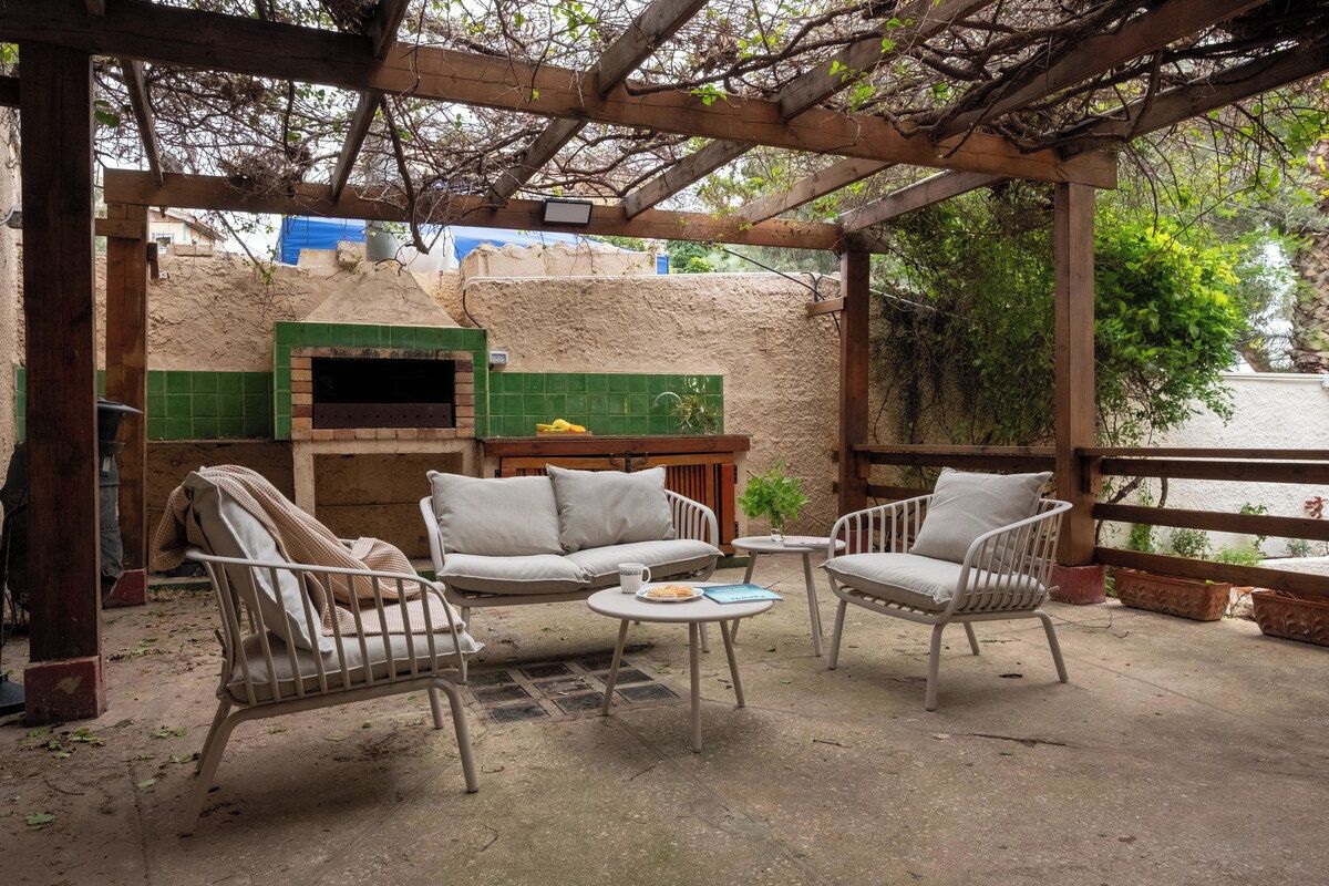 Une terrasse extérieure dotée d’une pergola en bois, d’un four en briques et d’un espace détente comprenant un canapé et deux fauteuils.