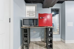 A compact kitchen with a microwave and a red refrigerator on a small wooden table.