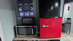 Una cocina con microondas, un refrigerador rojo y una ventana con mosquiteras.