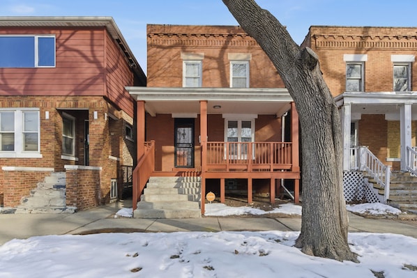 A row of brick townhouses with a central porch and steps leading to the entrance.