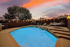 Patio con piscina, terraza de madera y mobiliario exterior.