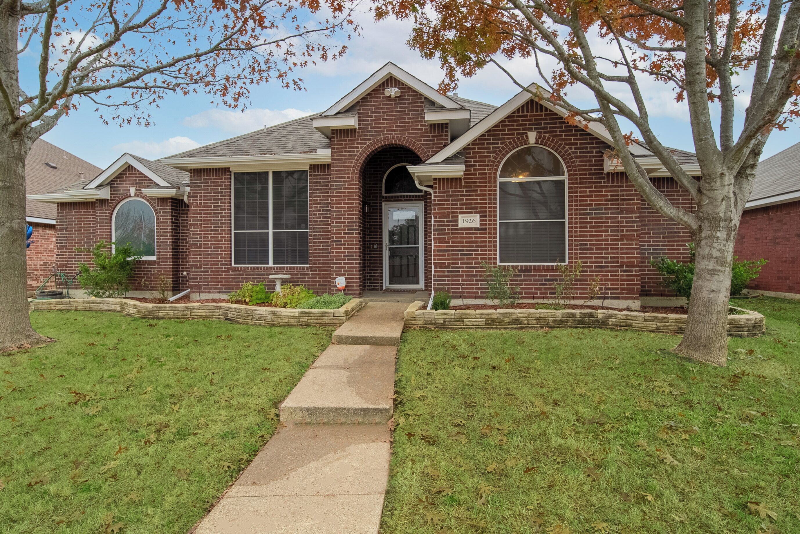 A two-story brick house with a front entrance, a small porch, and a well-maintained lawn.