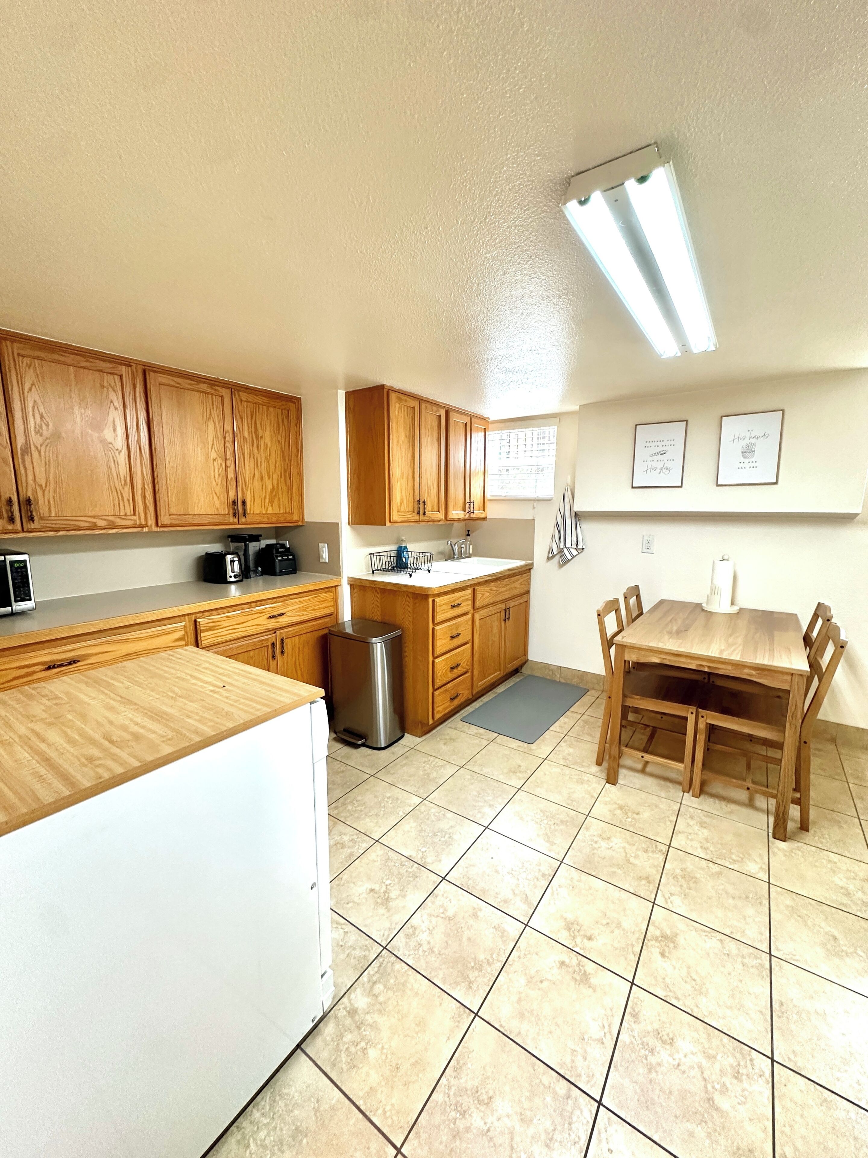 A kitchen with wooden cabinets, a stainless steel trash can, a coffee maker, and a dining table with chairs.