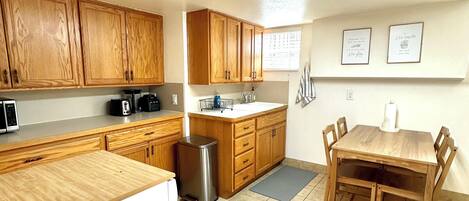 A kitchen with wooden cabinets, a stainless steel trash can, a coffee maker, and a dining table with chairs.