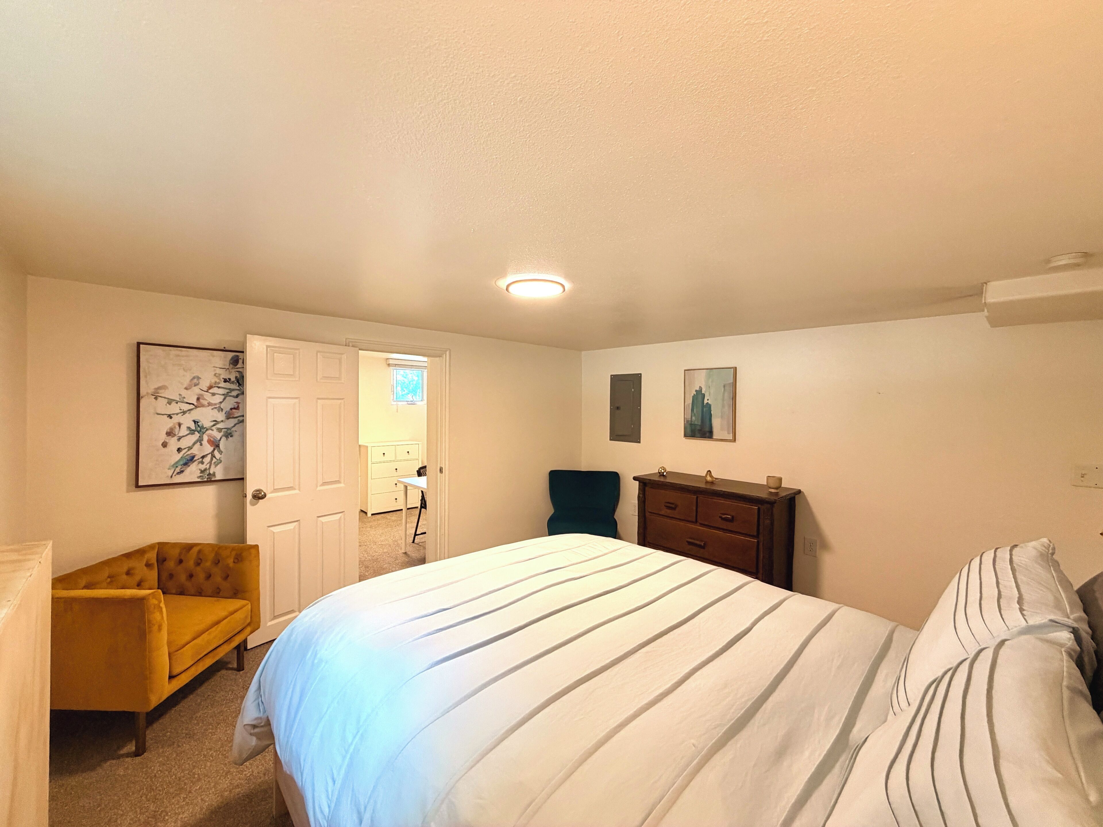 Ein Schlafzimmer mit einem Bett, einem Sessel, einer Kommode und einer Tür zu einem anderen Raum.