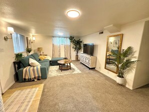 A living room with a sofa, a coffee table, a TV, and a mirror. - Stylish Bungalow Basement Apartment (Provo)