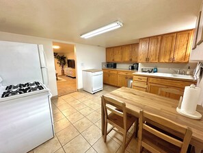 Una cocina con armarios de madera, un refrigerador blanco, una estufa, un microondas y una mesa de comedor con sillas.