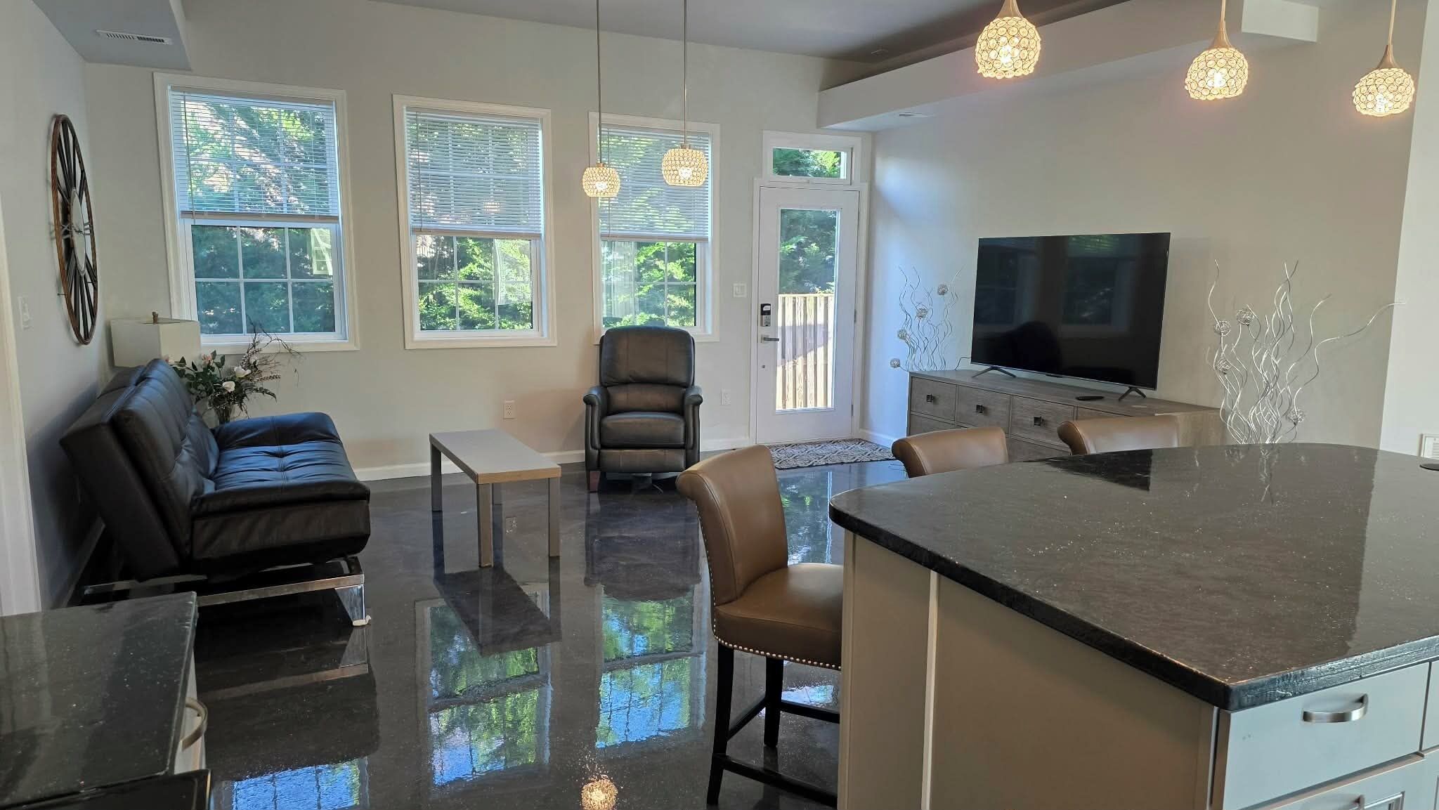 A modern kitchen with a large island, a dining area with a table and chairs, a seating area with a sofa, and a TV mounted on the wall.